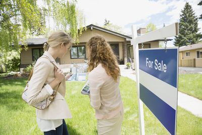 real estate agent and buyer standing in front of for sale sign