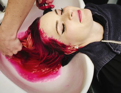 a hair salon client having red hair dye rinsed from her hair over a basin  664648969 5a8f87dd1f4e130036074afd