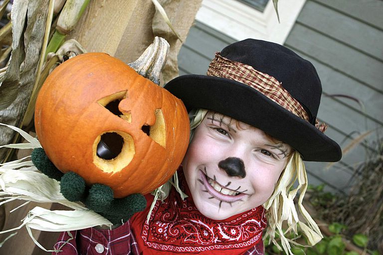 A kid dressed up as a scarecrow, holding a pumpkin.