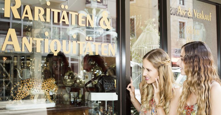 Two female friends standing in front of the window of an antique shop