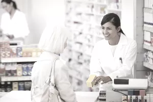Pharmacy technician handing medication to customer in drug store