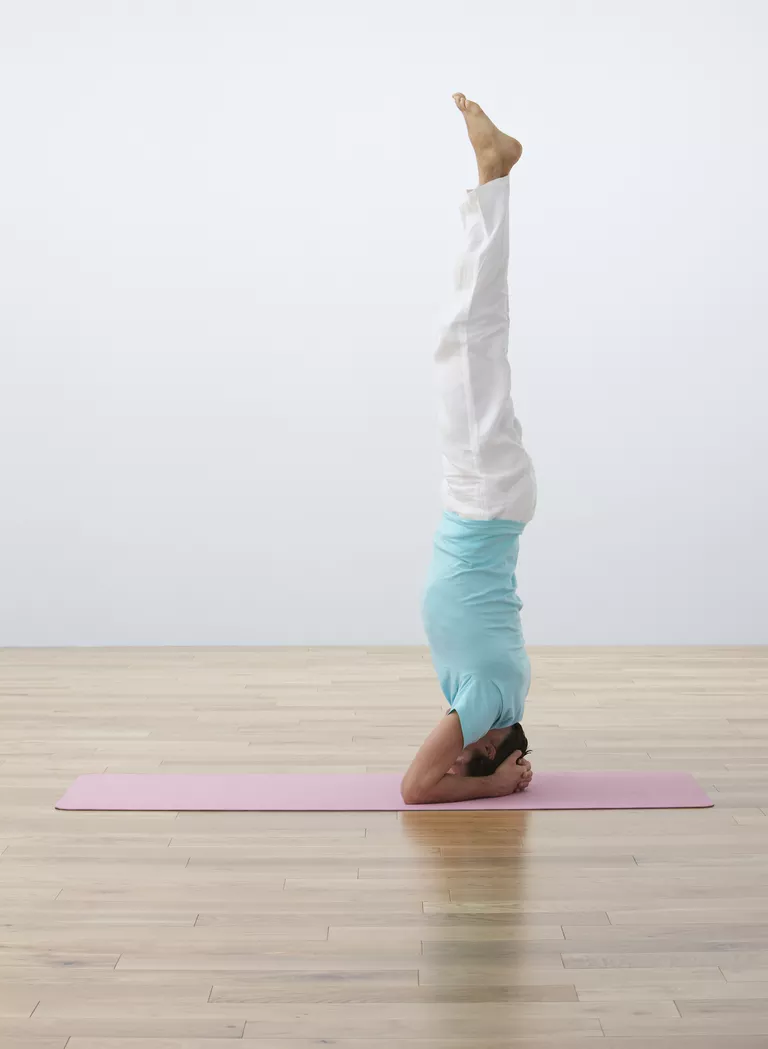 Man performing headstand on exercise mat, side view