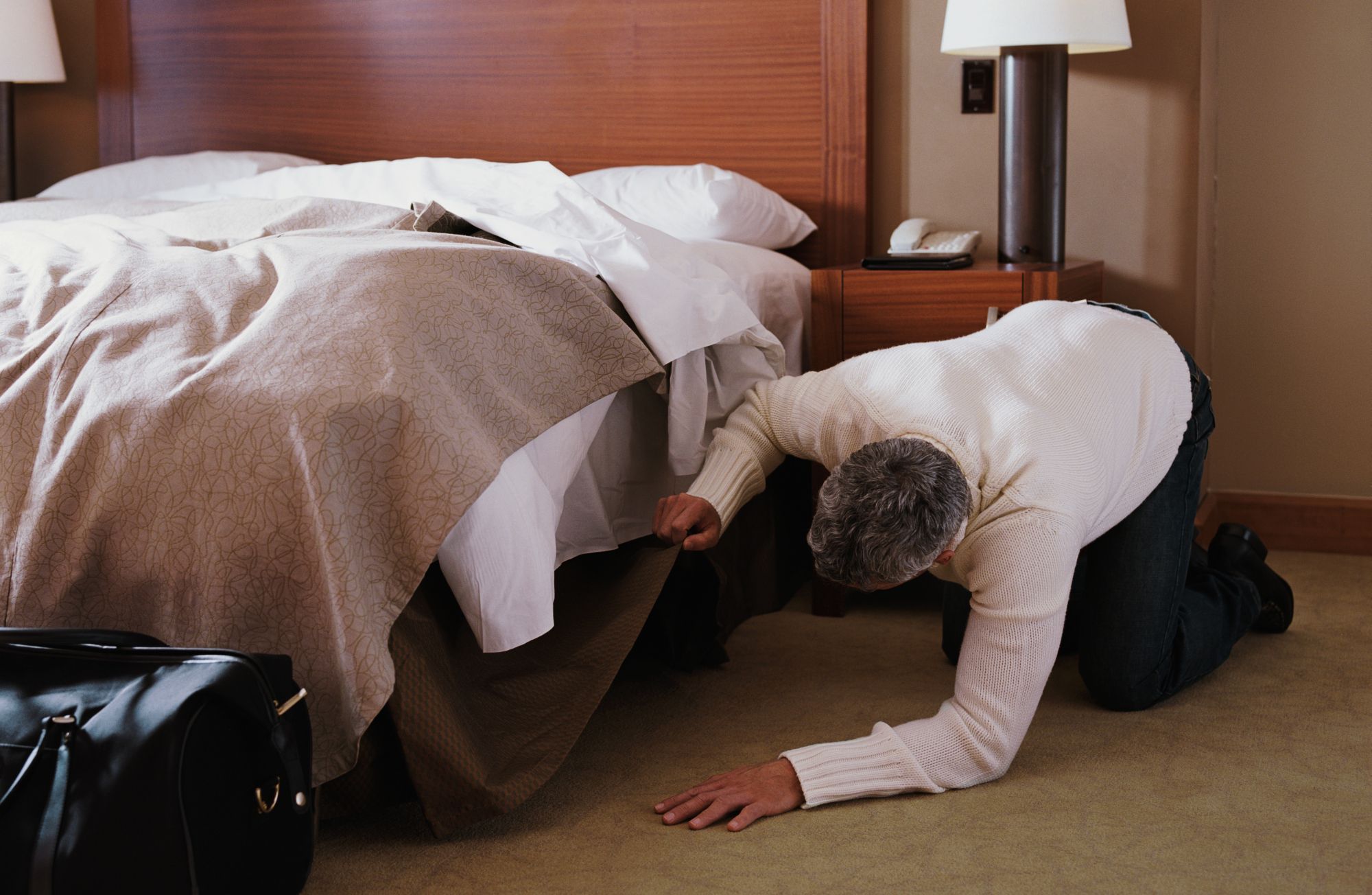 Сын залез в постель. Человек заглядывает под кровать. Ищет под кроватью. Случай в отеле.