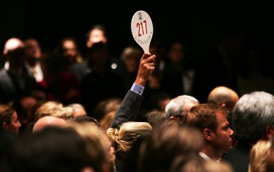 A man holds his hand up while bidding on a work of art inside the auction house Christie's