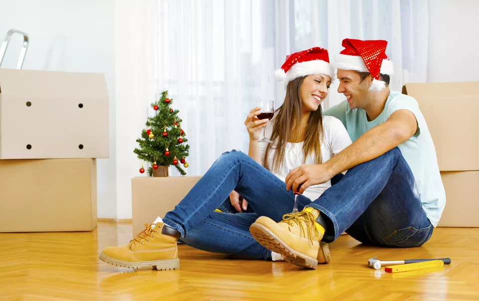 Happy couple wearing santa hats and surrounded by packed moving boxes