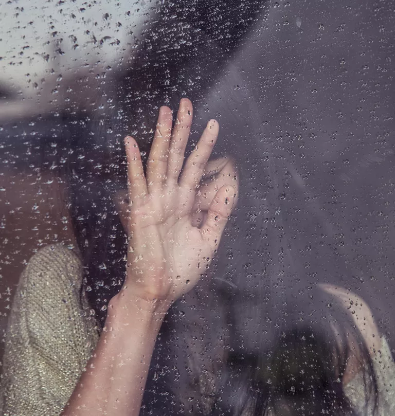 Woman leaning against rainy window