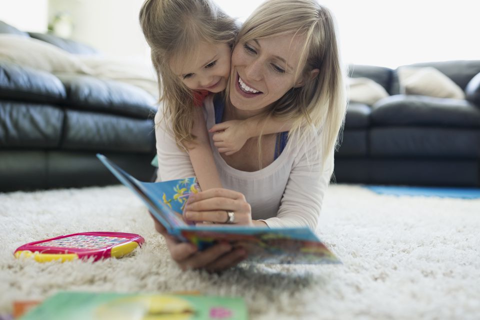 Daughter laying top mother reading book rug