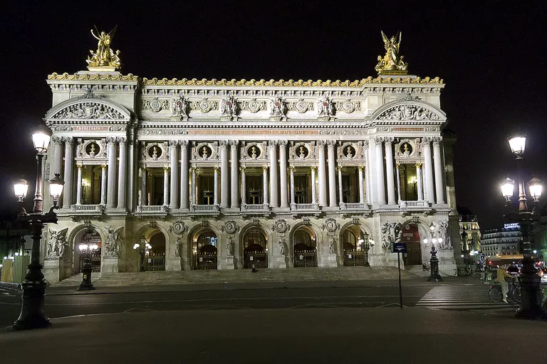 highly ornate exterior of rectangular box-shaped building with arches and columns and sculptures lit at night