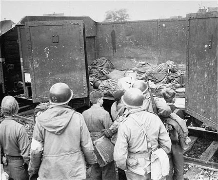 American soldiers force boys believed to be Hitler youth to examine boxcars containing bodies.