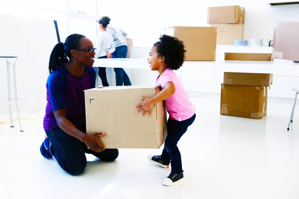Smiling mother helping toddler lift a packed moving box