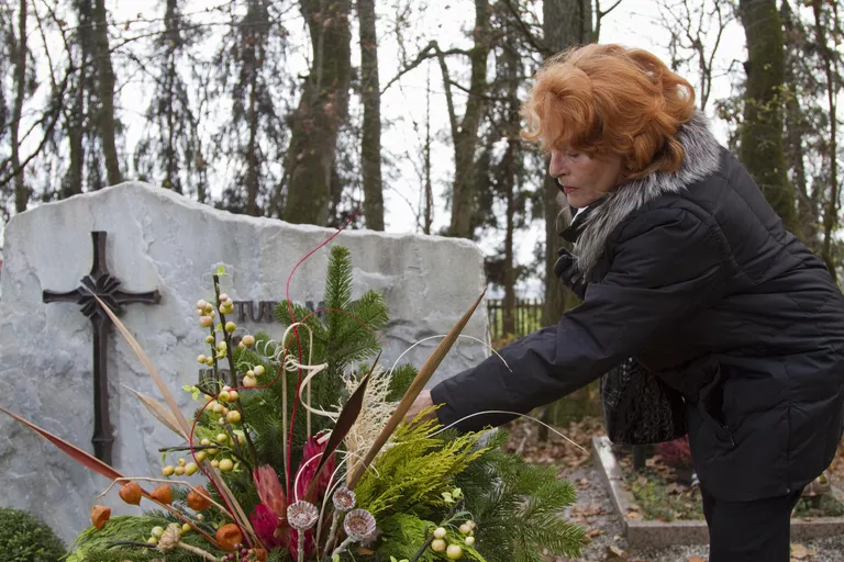 Senior woman placing flowers on grave in cemetery