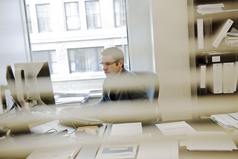 Business man seen through blinds works at computer