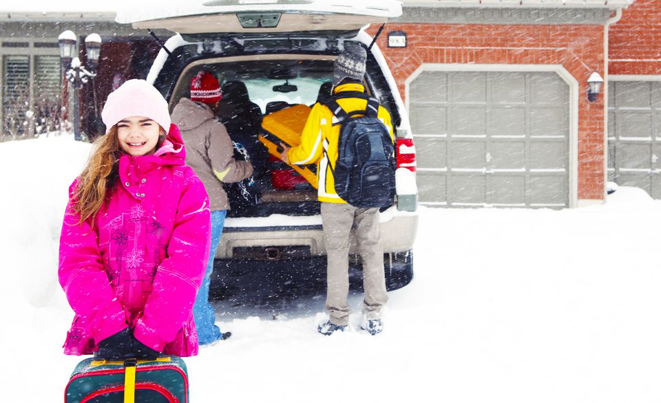 Young girl standing outside a packed car in the snow.