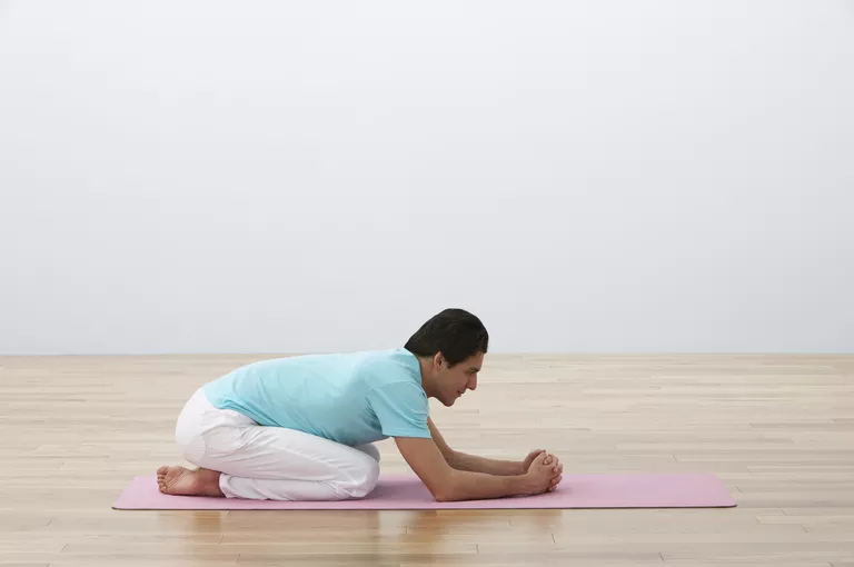 Man kneeling on exercise mat, leaning forward, side view