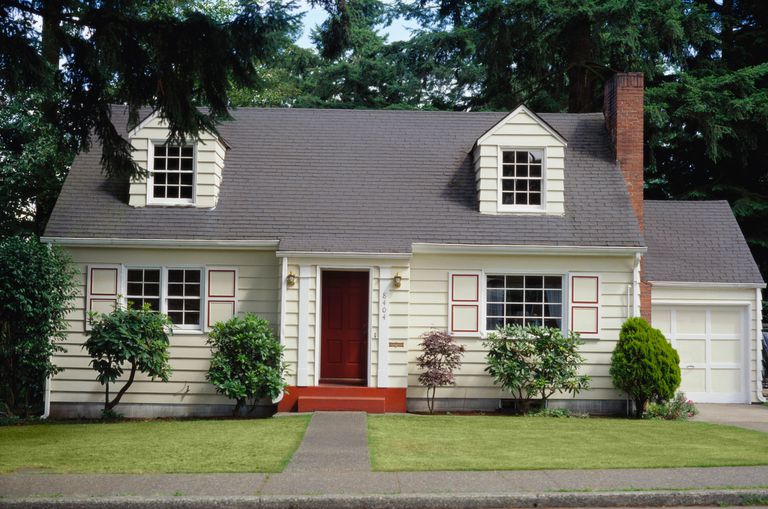 Facade of two-dormer, side chimney, 1-bay garage Cape Cod style home, with multi-paned windows with geometrically-patterned shutters