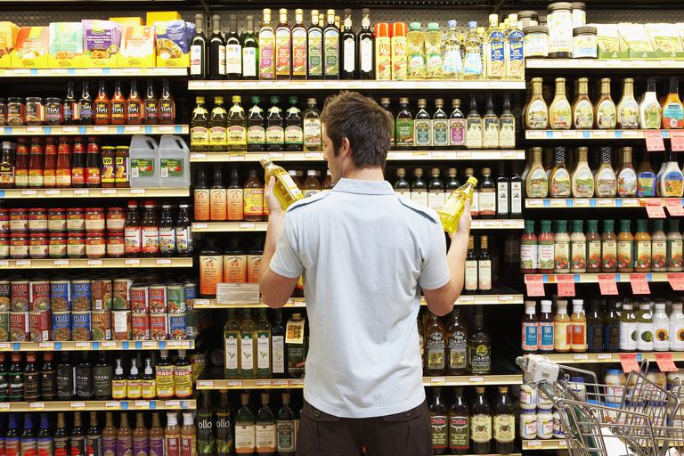 Young man in supermarket comparing bottles of oil, rear view, close-up