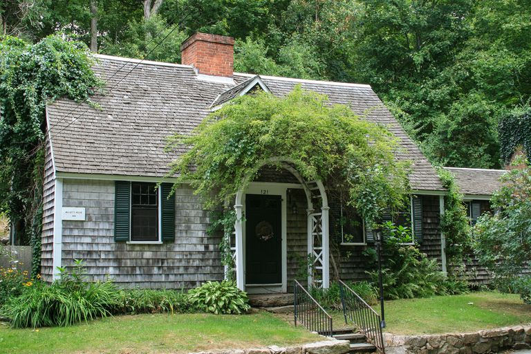 An arbor with vines hides a single centered dormer, center chimney, center door with one window to the left and two windows to the right