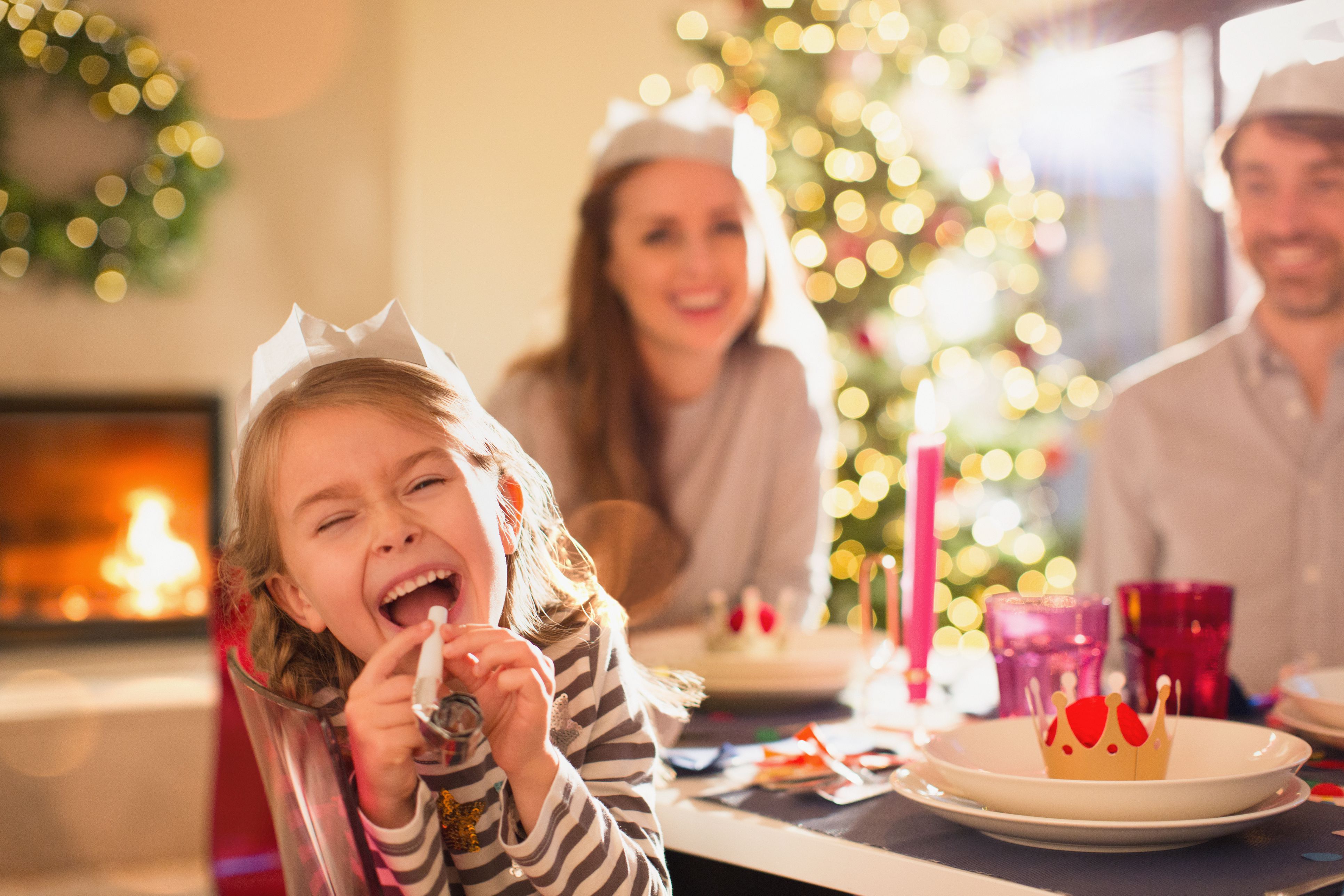 portrait playful girl in paper crown blowing party favor at christmas dinner table 59e65f e5a