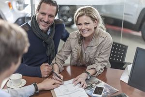 Couple signing sales contract at car dealership